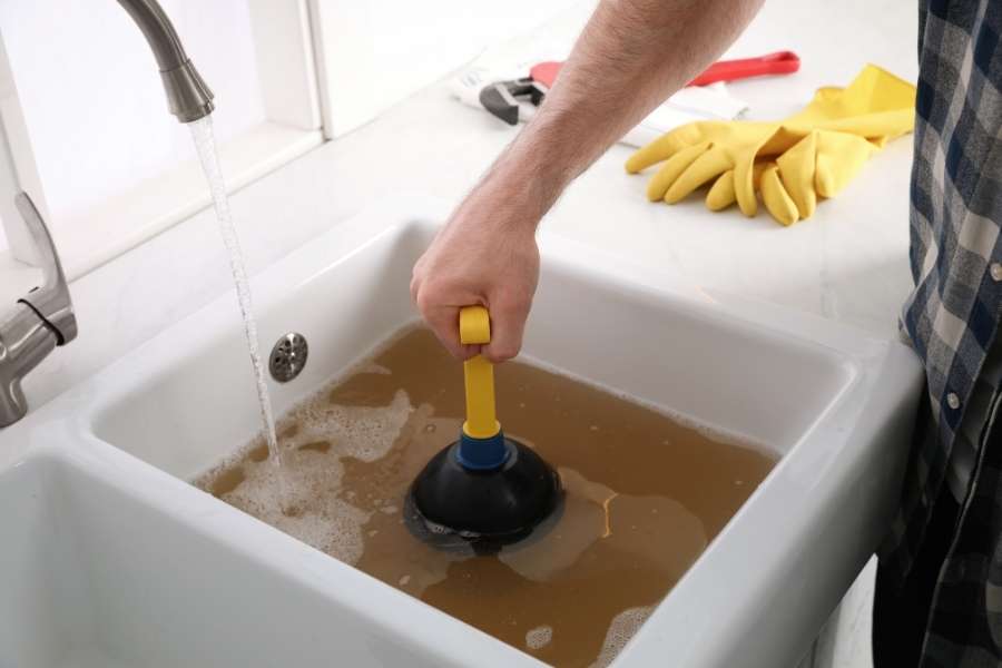 Une main utilise une ventouse pour déboucher un évier de cuisine rempli d'eau stagnante et sale.