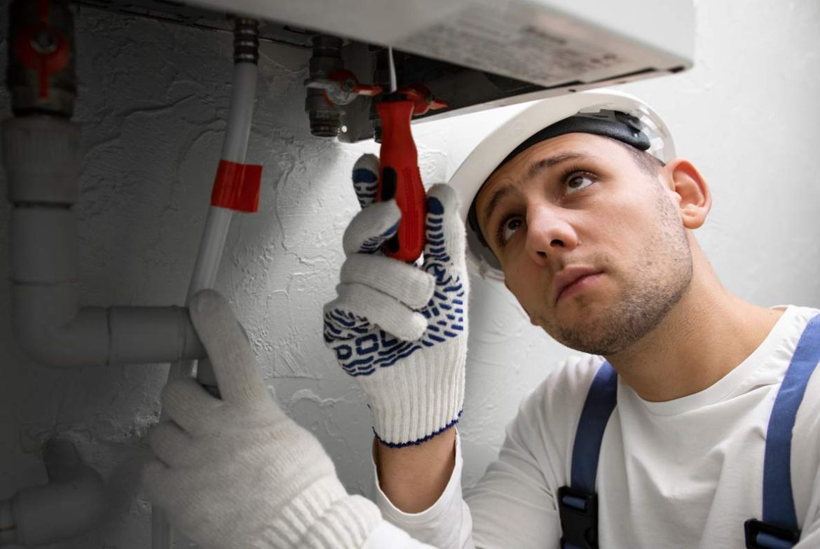 Un technicien en casque de chantier et gants effectue un dépannage chauffage urgence 24 7 sur une chaudière murale.
